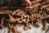 A child's hand reaches for the Fairy Cutter Set—Eco Playdough Tools, featuring wooden shapes like a heart, butterfly, flower, and bee on a textured brown blanket—perfect for inspiring sensory play or pairing with your favorite eco-friendly dough.