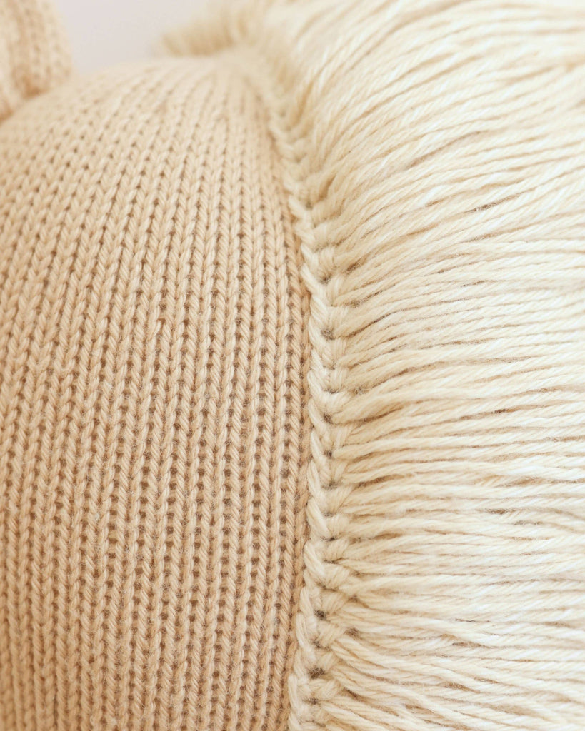 Close-up of the detailed texture and stitching of Cuddle + Kind Liam the Pony's beige knitted fabric next to cream-colored yarn fringes, showcasing this fair trade, handmade-in-Peru textile.