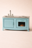 The Maileg Suitcasa Furnished Set (ships in one week) is a small blue toy kitchen with a sink, stovetop, and oven with a visible pie—ideal for Maileg mouse furniture. Features a plain, light-colored background.