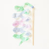 A wooden wand topped with a blue bead, adorned with Easter Basket Set streamer wand ribbons in pastel green, pink, and blue hues, arranged on a light background.