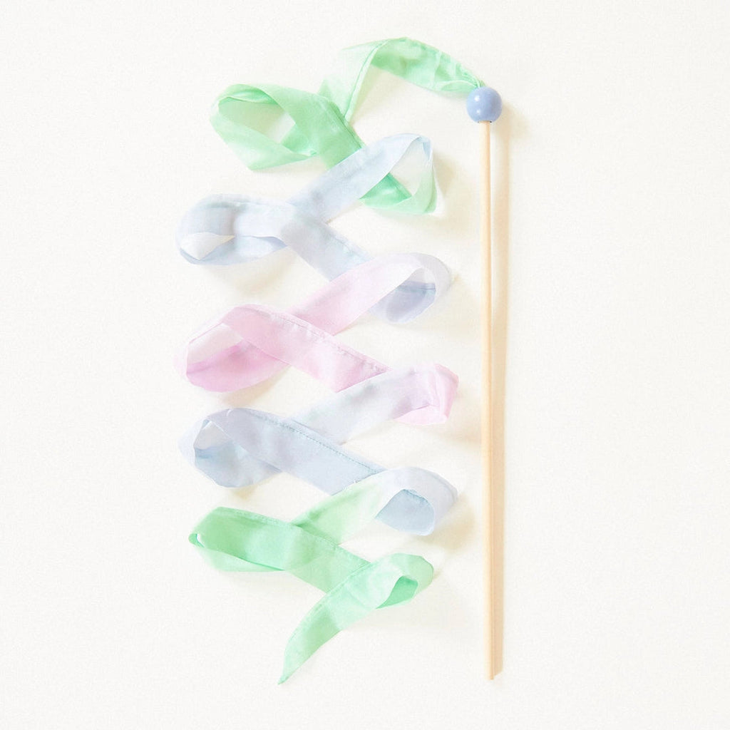A wooden wand topped with a blue bead, adorned with Easter Basket Set streamer wand ribbons in pastel green, pink, and blue hues, arranged on a light background.