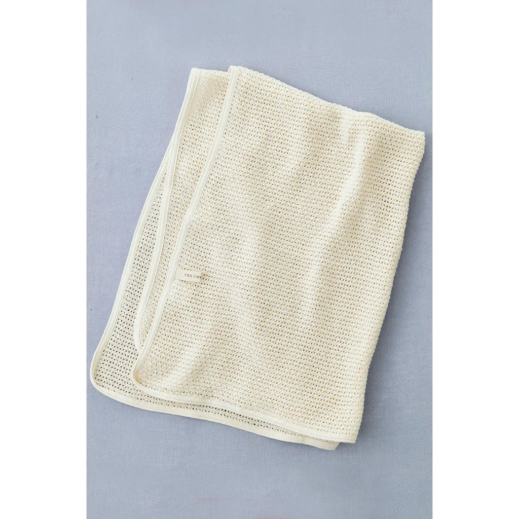 A neatly folded cream-colored Knit Baby Blanket is placed on a light gray surface. Crafted from Lithuanian cotton, this blanket features a textured weave and a clean, simple border. It's also machine washable for easy care.