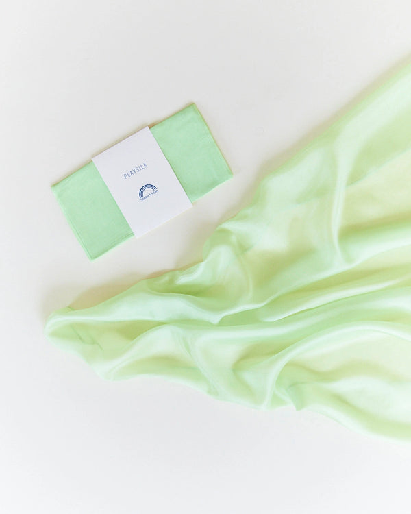 A mint green soap bar labeled "pleasure" placed next to a flowing, Sarah's Silk Playsilk - Lime on a soft white background.