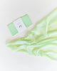 A mint green soap bar labeled "pleasure" placed next to a flowing, Sarah's Silk Playsilk - Lime on a soft white background.