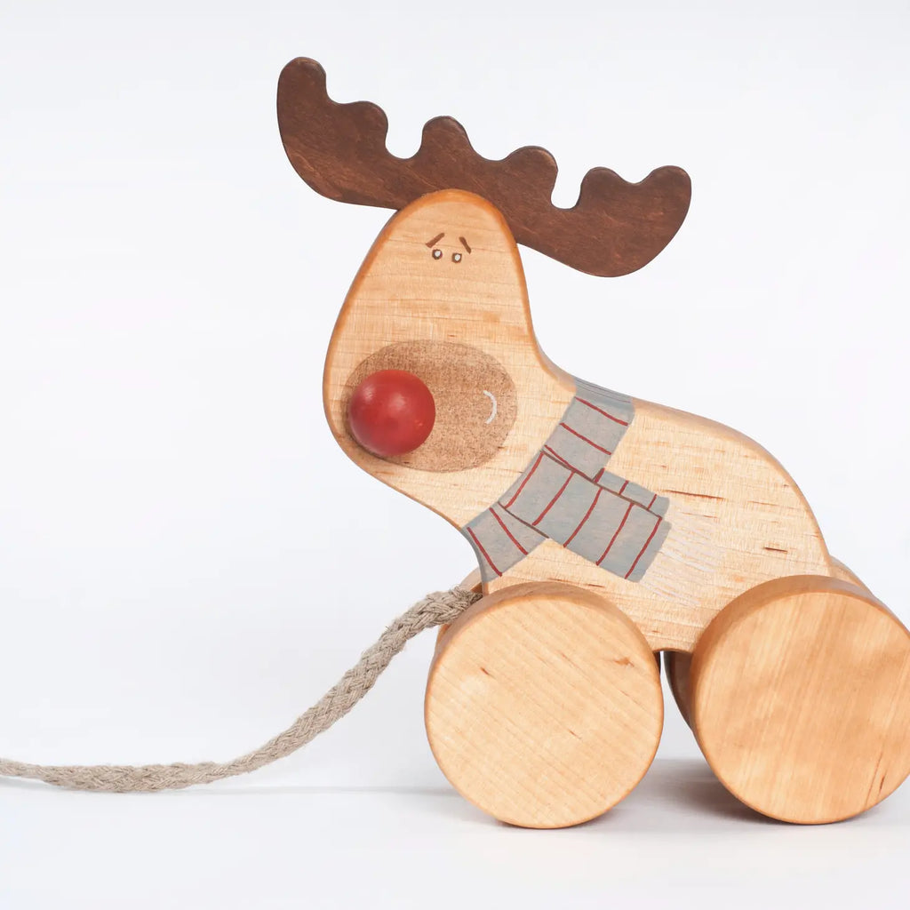 A Handmade Wooden Reindeer Pull Toy with large circular wheels, a red round nose, and a striped gray scarf around its neck. This sustainably sourced wooden playmate has a string attached, suggesting it can be pulled along. The reindeer boasts a playful and simplistic design, set against a white background.