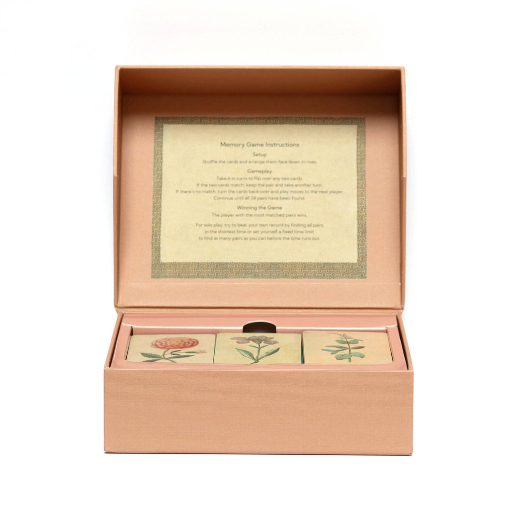 An open peach-colored box holds the Memory Game - Festival of Flowers, featuring illustrated watercolor flower cards. Game instructions are printed on the inside lid, and three floral cards can be seen inside the box.