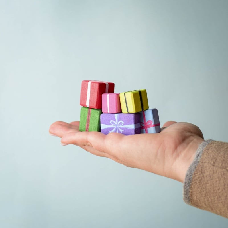 A hand holding several small, colorful boxes from the Bumbu Handmade Wooden Christmas Present Set against a light blue background—an ideal eco-friendly gift for Christmas.