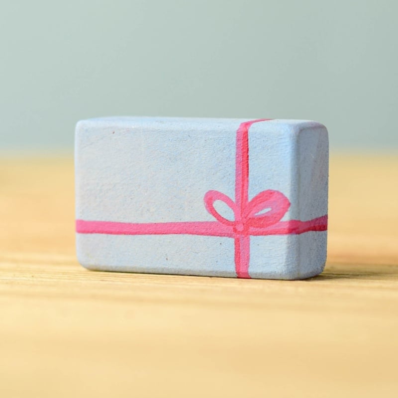 The Bumbu Handmade Wooden Christmas Present Set features a small, light blue rectangular block with a pink ribbon and bow design, resembling an eco-friendly wrapped gift—ideal for wooden gifts or as a Christmas present.