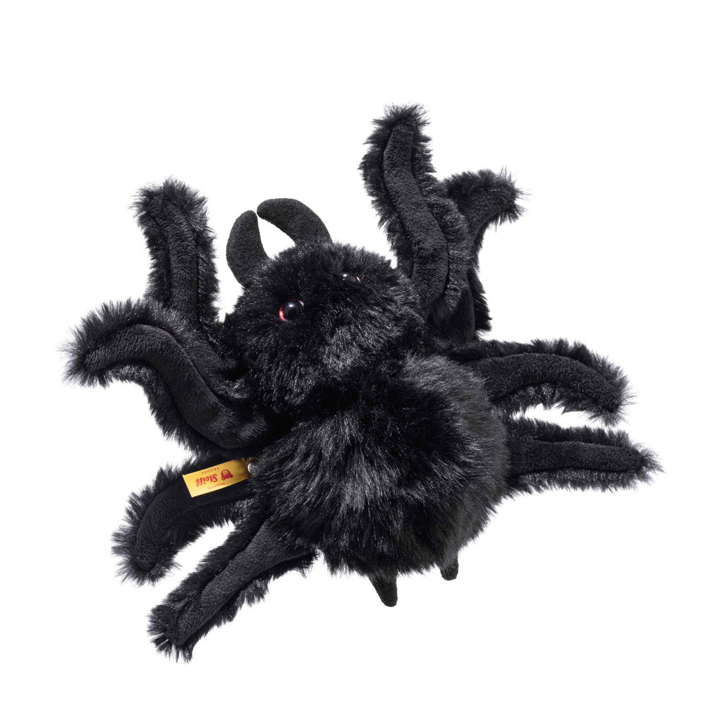 Steiff Cobweb the Spooky Spider is a fluffy black Halloween plush with eight legs, red eyes, and a soft, shaggy texture. Part of the Halloween Friends collection, it has a yellow tag on one leg and is shown on a white background.