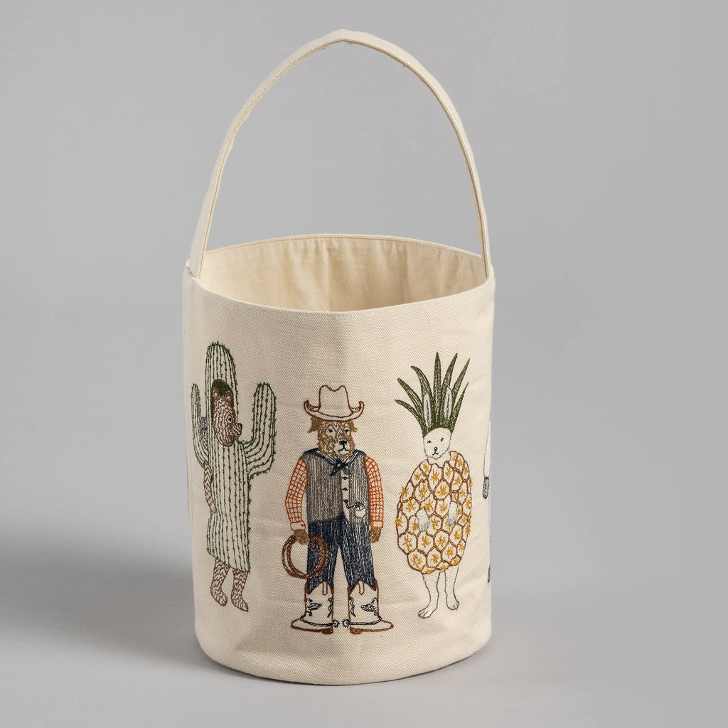 A Trick or Treat Small Bucket featuring embroidered designs of anthropomorphic plants: a cactus, a cowboy onion, and a pineapple, all standing upright like humans, alongside an embroidered tissue cover.