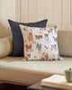 An embroidered Coral & Tusk Dogs and Toys Pillow with a variety of dog breed illustrations on it, placed on a beige sofa next to a dark blue pillow, in a cozy room setting.