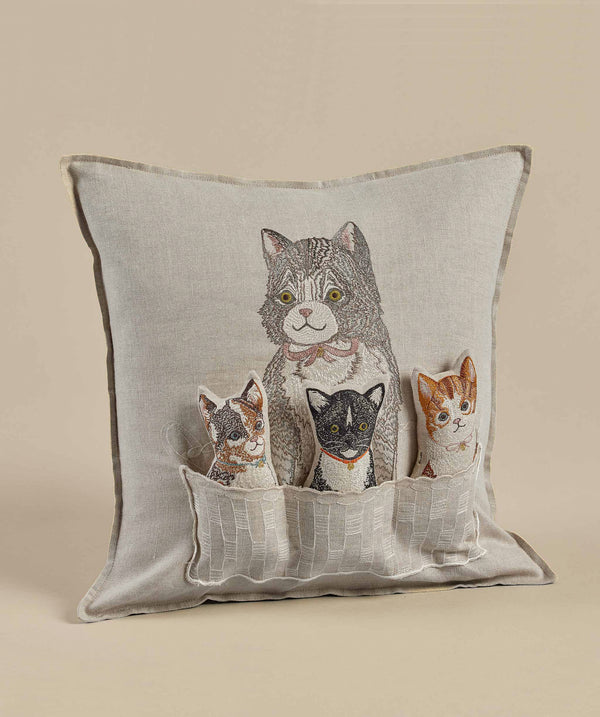 Decorative pillow featuring an embroidered design of a large grey cat and three smaller kittens of various colors peeking out from a Coral & Tusk Basket of Kittens Pocket Pillow, set against a neutral beige background.