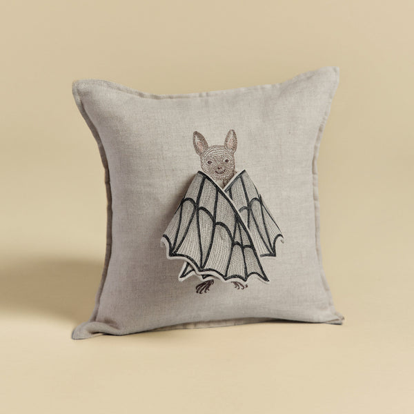 A Bat Wing Surprise Pillow with a beige background featuring an embroidered design of a bat with butterfly wings, showcasing detailed stitching on a neutral-toned fabric.