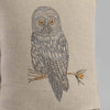 A detailed embroidery of a Coral & Tusk Great Grey Owl perched on a branch, featured on a beige linen fabric cushion cover. The owl has large, prominent eyes and intricate feather patterns.