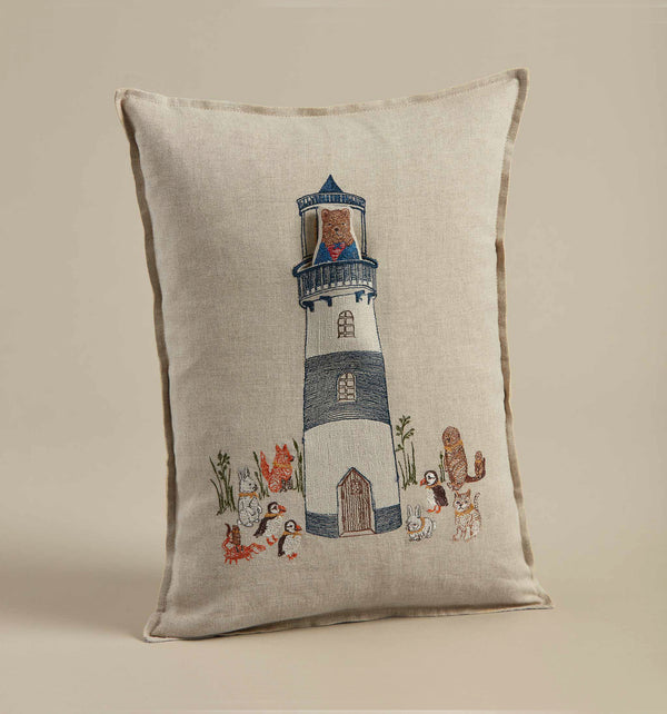 Decorative pillow featuring an embroidered design of a Coral & Tusk Lighthouse Friends Pocket Pillow surrounded by marine life and animals on a beige linen pillow cover.