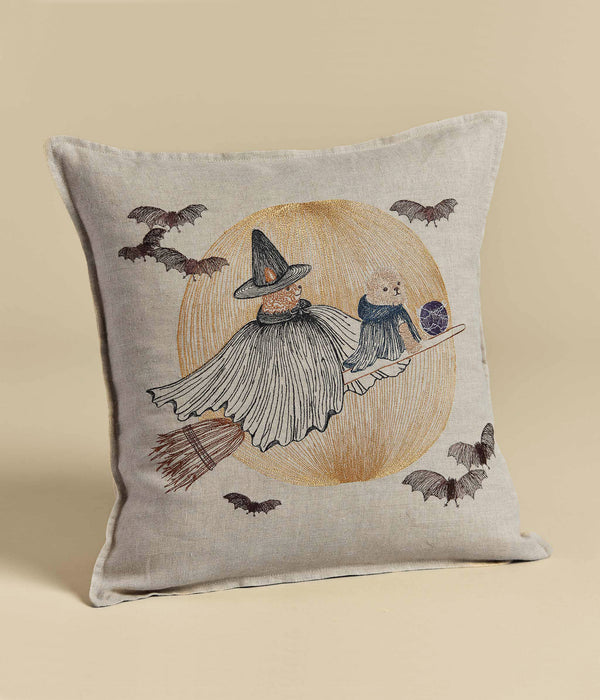 Decorative Supermoon Spell Pillow featuring an illustration of a witch and bear on a broom surrounded by flying bats, set against a beige background with a circular golden motif.