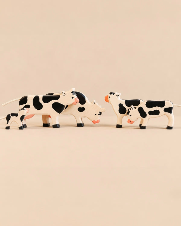 Four Holztiger Handmade Wooden Black & White Cow Family Set figurines of varying sizes standing on a light surface, ideal for imaginative play.
