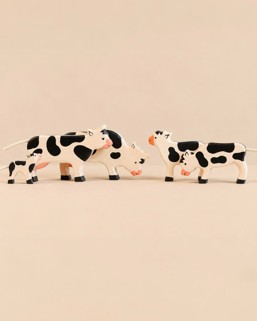 Four Holztiger Handmade Wooden Black & White Cow Family Set figurines of varying sizes standing on a light surface, ideal for imaginative play.