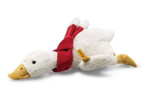 A cozy companion, the Steiff Gilda Christmas Goose plush lies on its stomach, featuring a white body, yellow beak and feet, and a festive red scarf.