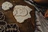 Cat-shaped dough is pressed and cut on a wooden surface, surrounded by more dough and the Pet Friends Faces Cutter Set - Eco Playdough Tool, with part of a person’s hand nearby. A striped cloth lies beneath the board, evoking the creativity and sensory play associated with using these eco-friendly playdough tools.