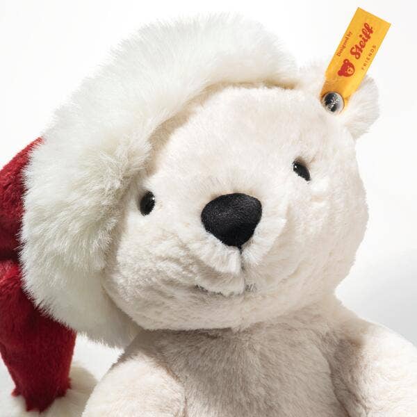 The Steiff Cozy Christmas Rico Polar Bear, marked with a yellow Steiff tag, wears a plush red and white Santa hat and smiles gently, bringing festive cheer to any space.