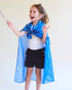 A young child smiles, holding a wand and wearing Sarah's Silks Enchanted Playsilk - Starry Night cape with stars and moons over a white shirt and black shorts—perfect for open-ended play against a plain background.