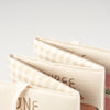 Close-up of three fabric-covered books, including the Little Farm Soft Book with beige and cream checkered and illustrated covers, fanned out on a white background—ideal as a baby gift.