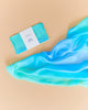 A folded Sarah's Silks Enchanted Playsilk - Sea, wrapped in a white band, rests next to a loosely draped matching scarf on a light beige background, inviting open-ended play.