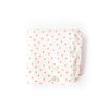 The Organic Baby Blanket – Little Peach is a white, GOTS-certified cotton blanket featuring small peach-shaped orange patterns and rounded corners, shown neatly folded against a plain white background.