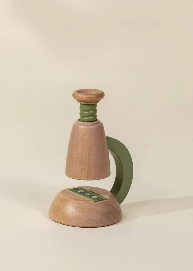 The Little Scientist Wooden Microscope is a modern, minimalist science toy for kids with green accents, a rounded base, curved handle, and cylindrical top, shown on a neutral light background.