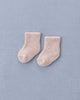 A pair of Baby Pile Knit Socks - Pink is placed side by side on a light blue textured fabric surface.