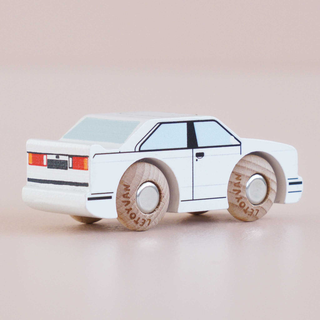 The No. 21 GT120 William | Made in England is a white wooden toy car featuring black accents and wooden wheels, displayed on a light surface and photographed from the rear left side.