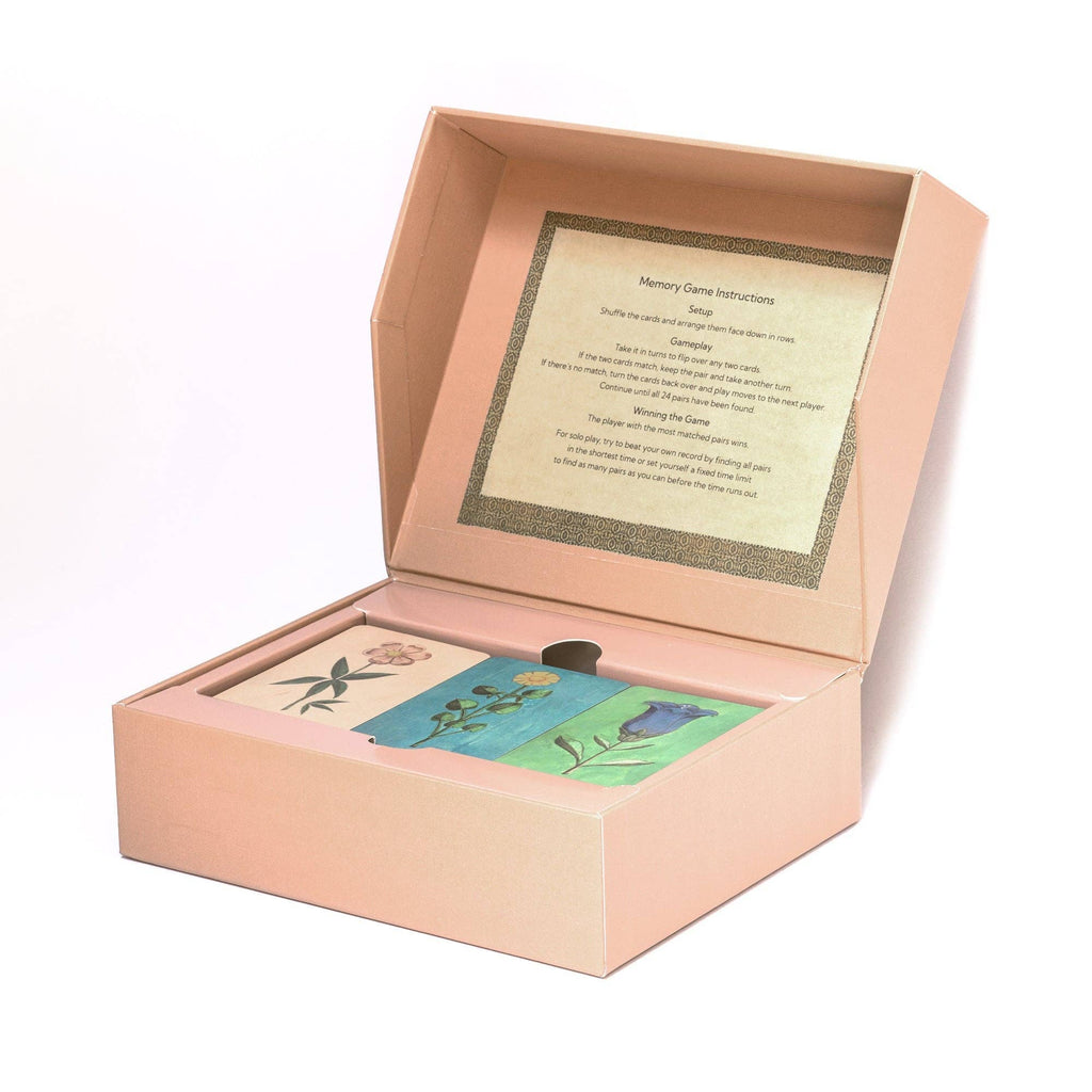 A pink box with a propped lid reveals the Memory Game - Festival of Flowers, a memory game featuring charming watercolor flower illustrations. The game's instructions are printed on the inner lid.