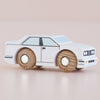 A small white wooden racing car with black details and wooden wheels, the No. 21 GT120 William by Le Toy Van, is shown on a light surface, exuding the nostalgic appeal of a classic retro toy—proudly made in England.