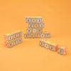 A pyramid of Uncle Goose Classic ABC Blocks with numbers and mathematical symbols on them, arranged on an orange background, with scattered blocks around it.