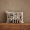 The Coral & Tusk Three Little Bears Pocket Pillow, featuring an embroidered cottage scene, sits against a tan wall with five charming, decorative cat figurines arranged on a rustic wooden surface. Ships in one week.