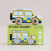 A wooden police car with blue and yellow checkered details, inspired by classic British patrol vehicles, is displayed atop a green box labeled “No. 40 GT250 Bobby | Made in England.” The box features an illustration of the police car alongside eco-friendly icons—making it perfect for imaginative play.