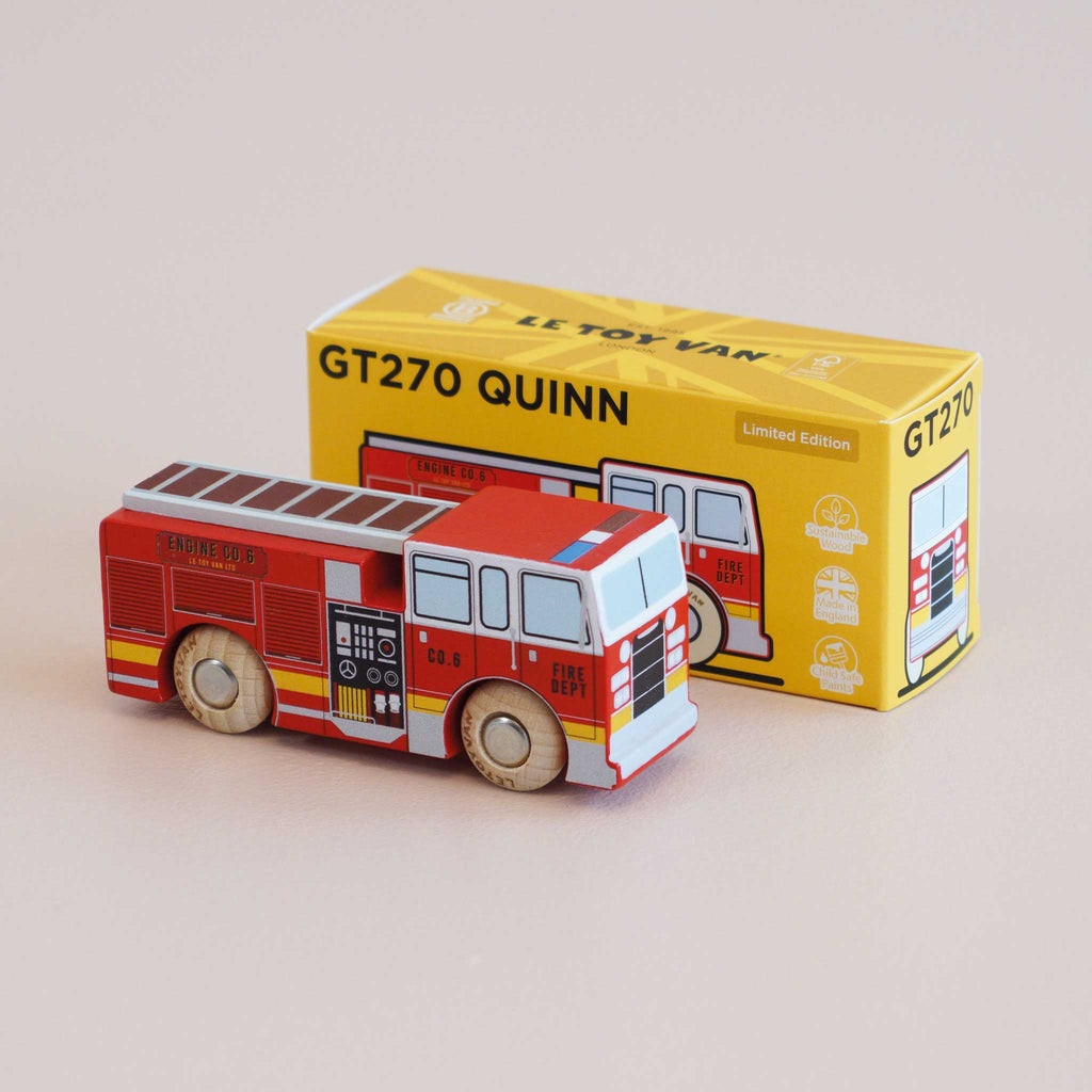 A small wooden fire engine sits in front of its yellow box, which features an illustration of the same fire engine and the text “No. 44 GT270 Quinn | Made in England.” Perfect for imaginative adventures and daring rescue missions, this charming toy sparks endless creative play.