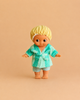 The Minikane Mini Pancha Doll - Basile with Green Striped Bath Set features a big-eyed doll dressed in a yellow shower cap, green robe, and striped shorts, standing barefoot on a beige background—perfect for imaginative play.