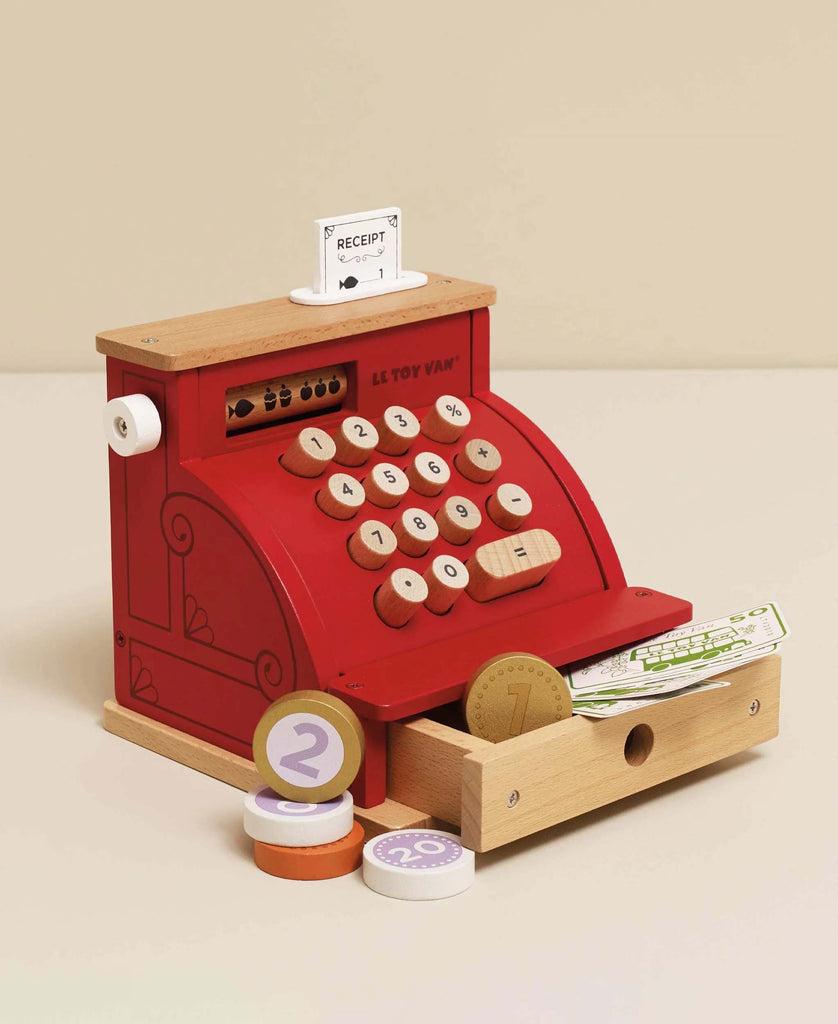 The Cash Register & Money is a red wooden pretend playset with large numbered buttons, a receipt, and play coins and bills. The open drawer shows wooden coins. Perfect for educational fun, set against a plain beige background.