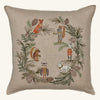 The Coral & Tusk Tree Trimmers Wreath Pillow is a square beige Christmas pillow featuring embroidered woodland animals—fox, squirrel, rabbit, owl, chipmunk, and a white wolf—framed by a pine and cone holiday wreath.