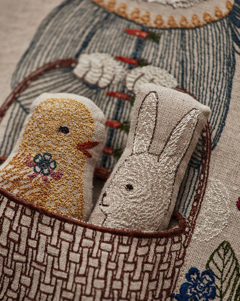 The Coral & Tusk Easter Bunny Pocket Pillow features embroidered fabric toys—a yellow chick and a white bunny dressed in blue—nestled in a brown-patterned pocket, making it a charming Easter decoration.