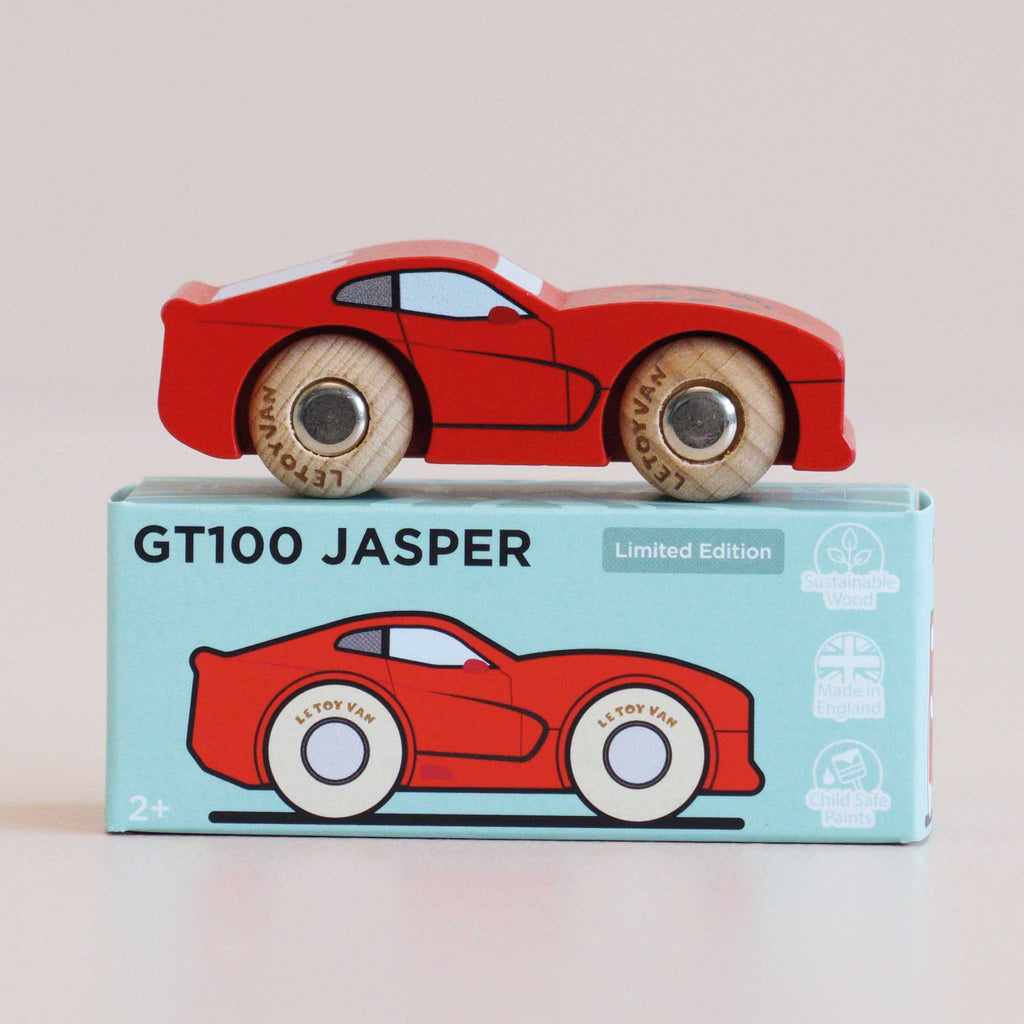 A red wooden sports car rests atop a blue box labeled “No. 18 GT100 Jasper | Made in England.” The box displays an illustration of the car along with icons denoting sustainable wood and child-safe paints, capturing the classic allure of performance motoring in an enduring toy.