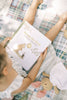A child sits on a quilt holding Winnie-the-Pooh: Finding Feelings, a board book about emotions for toddlers, with a plush doll nearby.