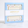 A rectangular Monopoly Bianco Edition board game box with a cutout window revealing a game board featuring property spaces in light neutral tones.