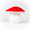 The Red Mushroom Lamp is a whimsical night light with a white stem and red cap featuring small white spots. Plugged in and set against a plain white background, it’s perfect as a nursery lamp or for any children's room.