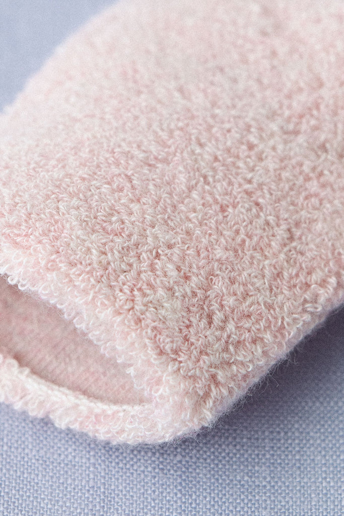 Close-up of a pink, fluffy fabric with a looped texture, resembling pile knitting or terrycloth material. The fabric appears soft and cozy, like Baby Pile Knit Socks - Pink, with the image focusing on the texture and weave of the material against a light purple background.