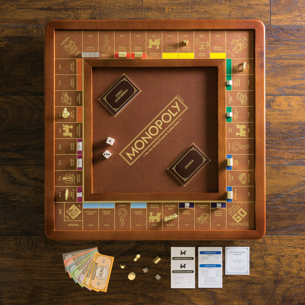 The Monopoly Luxury Edition, in brown and gold, is displayed on a wooden table with cards, die-cast metal tokens, paper money, and property cards neatly arranged for a premium board game experience.