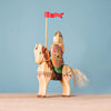The Bumbu Handmade Wooden Dacian Knight and Steed Set features a handcrafted wooden knight with a helmet, shield, and red flag riding a painted horse with a light mane—all set against a blue background.