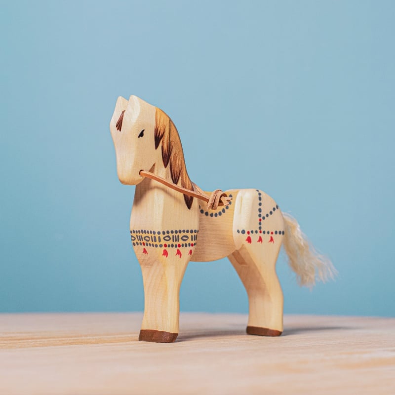 The Bumbu Handmade Wooden Dacian Knight and Steed Set features a painted, handcrafted steed with decorative patterns and a string tail, displayed on a light wooden surface against a plain blue background.